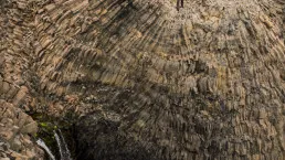 Escursionisti davanti a una cascata tra colonne di basalto
